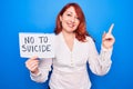 Young redhead woman asking for stop depression holding paper with not to suicide message smiling happy pointing with hand and