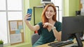 Young redhead woman business worker using computer make selfie by smartphone at office Royalty Free Stock Photo