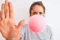 Young redhead woman chewing gum and blowing hair bubble over white isolated background with open hand doing stop sign with serious