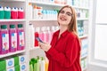 Young redhead woman customer smiling confident using smartphone at pharmacy