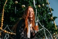 Young redhead woman drinking coffee wandering near Christmas tree in the streets on winter city. Happy young smiling Royalty Free Stock Photo