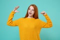 Young redhead woman girl in yellow sweater posing isolated on blue turquoise background studio portrait. People emotions