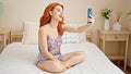 Young redhead woman having video call sitting on bed at bedroom Royalty Free Stock Photo