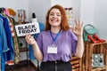 Young redhead woman holding black friday banner at retail shop doing ok sign with fingers, smiling friendly gesturing excellent Royalty Free Stock Photo