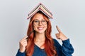 Young redhead woman holding books over head smiling happy pointing with hand and finger Royalty Free Stock Photo