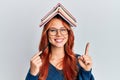 Young redhead woman holding books over head smiling with an idea or question pointing finger with happy face, number one Royalty Free Stock Photo