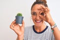 Young redhead woman holding cactus plant pot over isolated background with happy face smiling doing ok sign with hand on eye Royalty Free Stock Photo