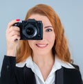 Young redhead woman holding a camera. She is wearing a suit. Royalty Free Stock Photo