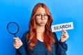 Young redhead woman holding magnifying glass and search word depressed and worry for distress, crying angry and afraid