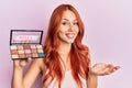 Young redhead woman holding makeup nudes celebrating achievement with happy smile and winner expression with raised hand