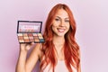 Young redhead woman holding makeup nudes looking positive and happy standing and smiling with a confident smile showing teeth