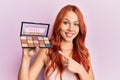 Young redhead woman holding makeup nudes smiling happy pointing with hand and finger