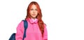 Young redhead woman holding student backpack and books thinking attitude and sober expression looking self confident