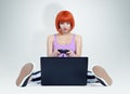 Young redhead woman with joystick sits on the floor in front of a laptop. Gamer plays