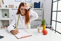 Young redhead woman nutritionist doctor at the clinic making fun of people with fingers on forehead doing loser gesture mocking Royalty Free Stock Photo