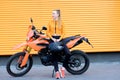 Young redhead woman with orange lipstick colored lips, weared orange sports jacket, standing near orange enduro motorcycle with Royalty Free Stock Photo