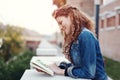 Young redhead woman reading book outdoors in park at autumn, smiling, profile view Royalty Free Stock Photo
