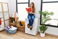 Young redhead woman reading book waiting for washing machine at laundry room Royalty Free Stock Photo