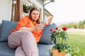 Young redhead woman relaxing with phone in the yard of the house in summer. Negative people emotion. Upset 30s women is