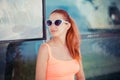 The young redhead woman sitting at the bus stop she expects the bus outdoors. Stylish girl in casual pink shirt, in butterfly Royalty Free Stock Photo