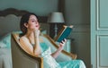 Young redhead woman sitting in chair reading book. Royalty Free Stock Photo