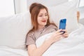 Young redhead woman using smartphone lying on bed at bedroom Royalty Free Stock Photo