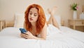Young redhead woman using smartphone lying on bed at bedroom Royalty Free Stock Photo