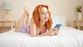 Young redhead woman using smartphone lying on bed at bedroom Royalty Free Stock Photo