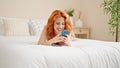 Young redhead woman using smartphone lying on bed at bedroom Royalty Free Stock Photo