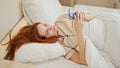 Young redhead woman using smartphone lying on bed at bedroom Royalty Free Stock Photo