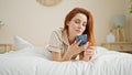 Young redhead woman using smartphone lying on bed at bedroom Royalty Free Stock Photo