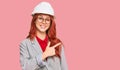 Young redhead woman wearing architect hardhat cheerful with a smile of face pointing with hand and finger up to the side with Royalty Free Stock Photo