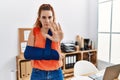 Young redhead woman wearing arm on sling at the office with open hand doing stop sign with serious and confident expression, Royalty Free Stock Photo