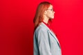 Young redhead woman wearing business jacket and glasses looking to side, relax profile pose with natural face with confident smile Royalty Free Stock Photo