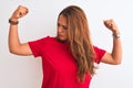 Young redhead woman wearing red casual t-shirt stading over white isolated background showing arms muscles smiling proud Royalty Free Stock Photo