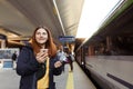 Young redhhead woman waiting on station platform with backpack on background electric train using smart phone. Railroad Royalty Free Stock Photo