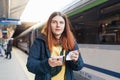 Young redhhead woman waiting on station platform with backpack on background electric train using smart phone. Railroad Royalty Free Stock Photo