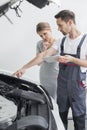 Young repair worker explaining car engine to worried customer in workshop Royalty Free Stock Photo