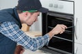 young repairman in overall installing brand new oven in kitchen