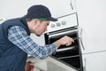 Young repairman in overall installing brand new oven in kitchen