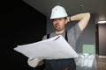 Young repairman standing in empty flat, looking at construction plan and feeling frustrated