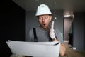 Young repairman standing in empty flat, looking at construction plan and feeling shocked