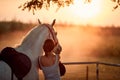 Young rider girl with her horse at sunset