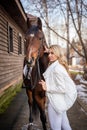 Young rider woman blonde with long hair in white clothes standing near brown horse Royalty Free Stock Photo