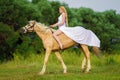 Rider woman blonde with long hair in a white dress with a train posing on a palamino horse Royalty Free Stock Photo