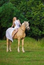 Rider woman blonde with long hair in a white dress with a train posing on a palamino horse