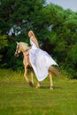 Rider woman blonde with long hair in a white dress with a train posing on a palamino horse Royalty Free Stock Photo