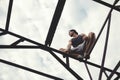 Young risky guy balancing and sitting on the top of high metal construction Royalty Free Stock Photo