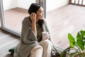 Young romantic asian woman enjoying weekend, relaxing morning with cup of tea, sitting on floor near window and looking Royalty Free Stock Photo