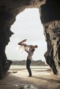 Young romantic couple dancing through rock archway at the beach